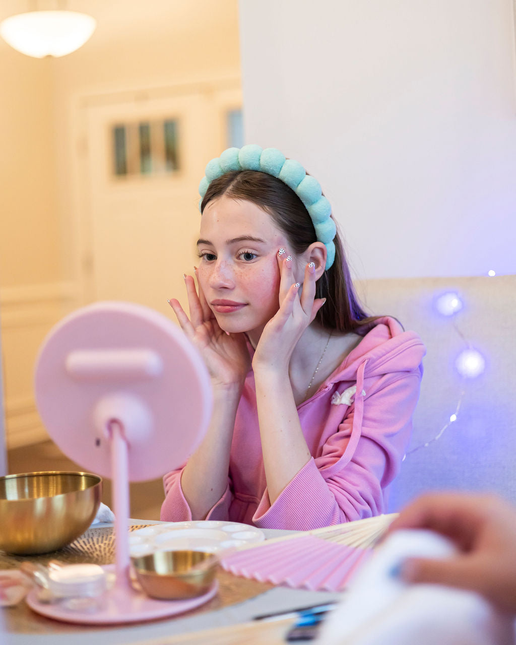 Girl applying skincare in front of a mirror with colorful lights in the background