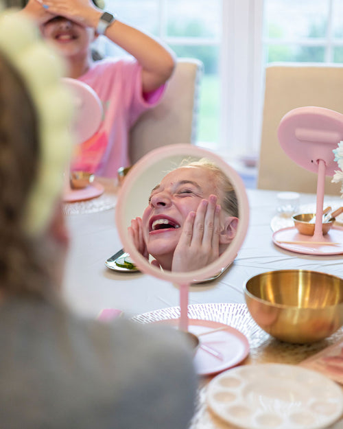 Person applying skincare in front of a mirror with another person in the background.