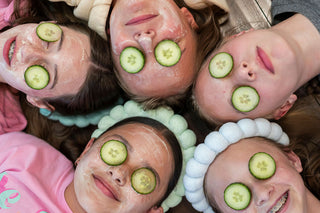 Children with cucumber slices on their eyes lying on a wooden floor.
