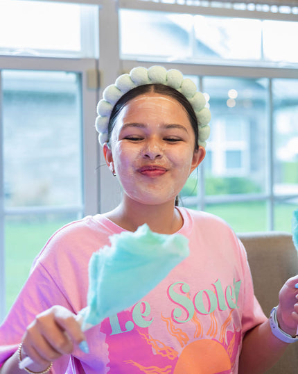 Person wearing a pink shirt with 'Le Soleil' text, holding cotton candy indoors.
