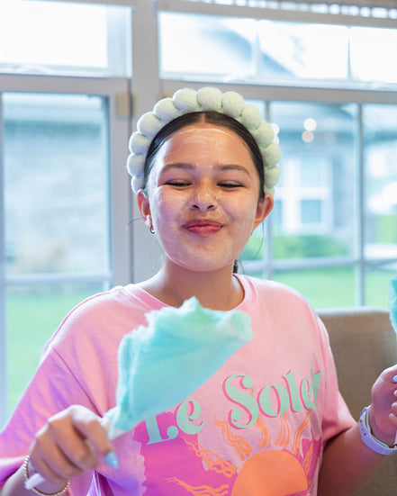 Person wearing a pink shirt with 'Le Soleil' text, holding cotton candy indoors.