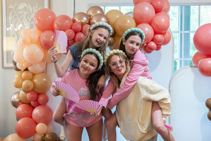 Group of young women celebrating with pink and gold balloons in a decorated room.