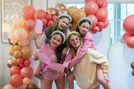 Group of young women celebrating with pink and gold balloons in a decorated room.